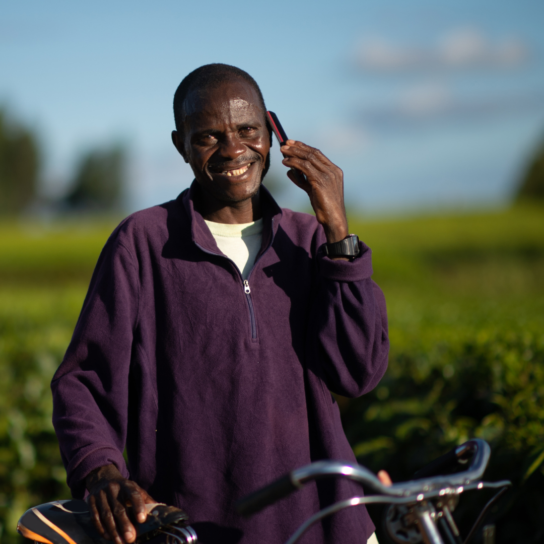Man with a bicycle looking at camera talking on a mobile phone in a rural setting