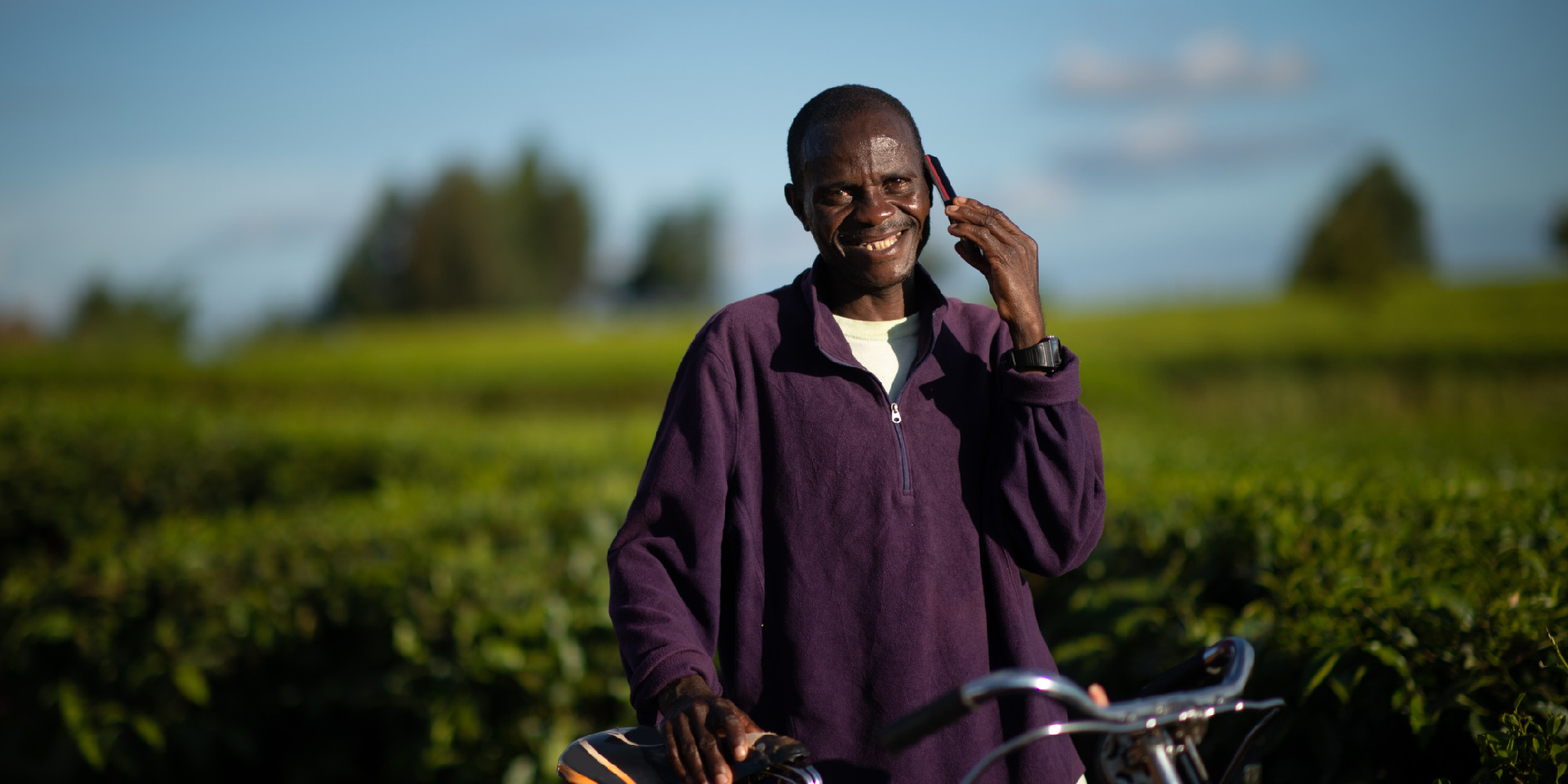 Man with a bicycle looking at camera talking on a mobile phone in a rural setting