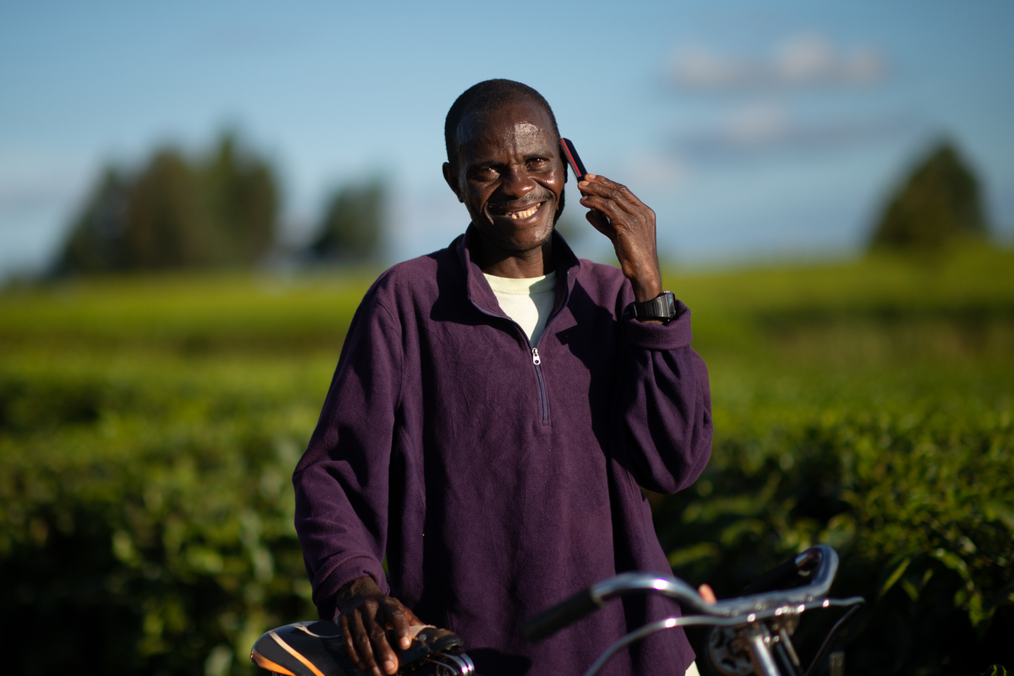 Man with a bicycle looking at camera talking on a mobile phone in a rural setting