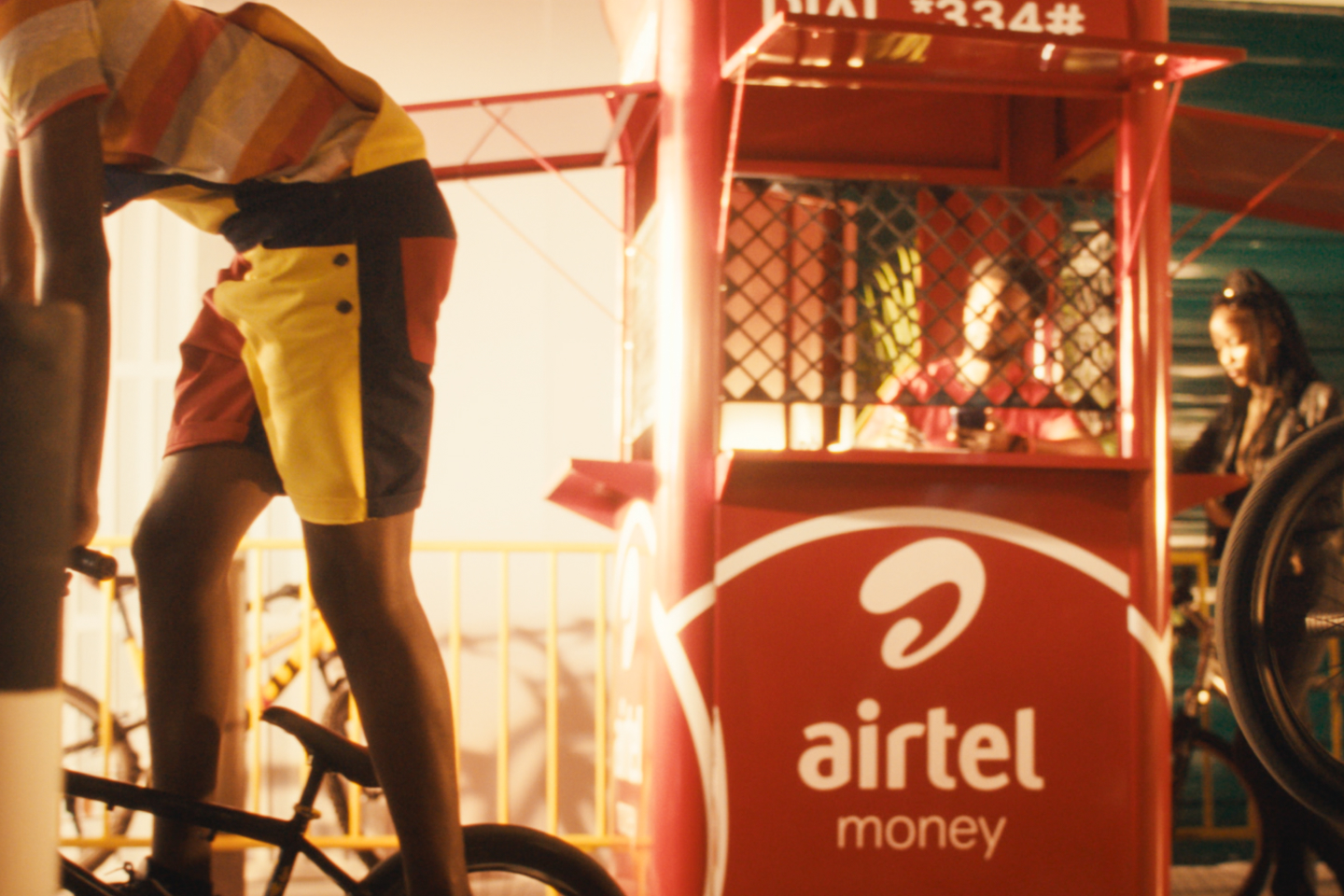 Customers at an Airtel Money kiosk with cyclist in foreground