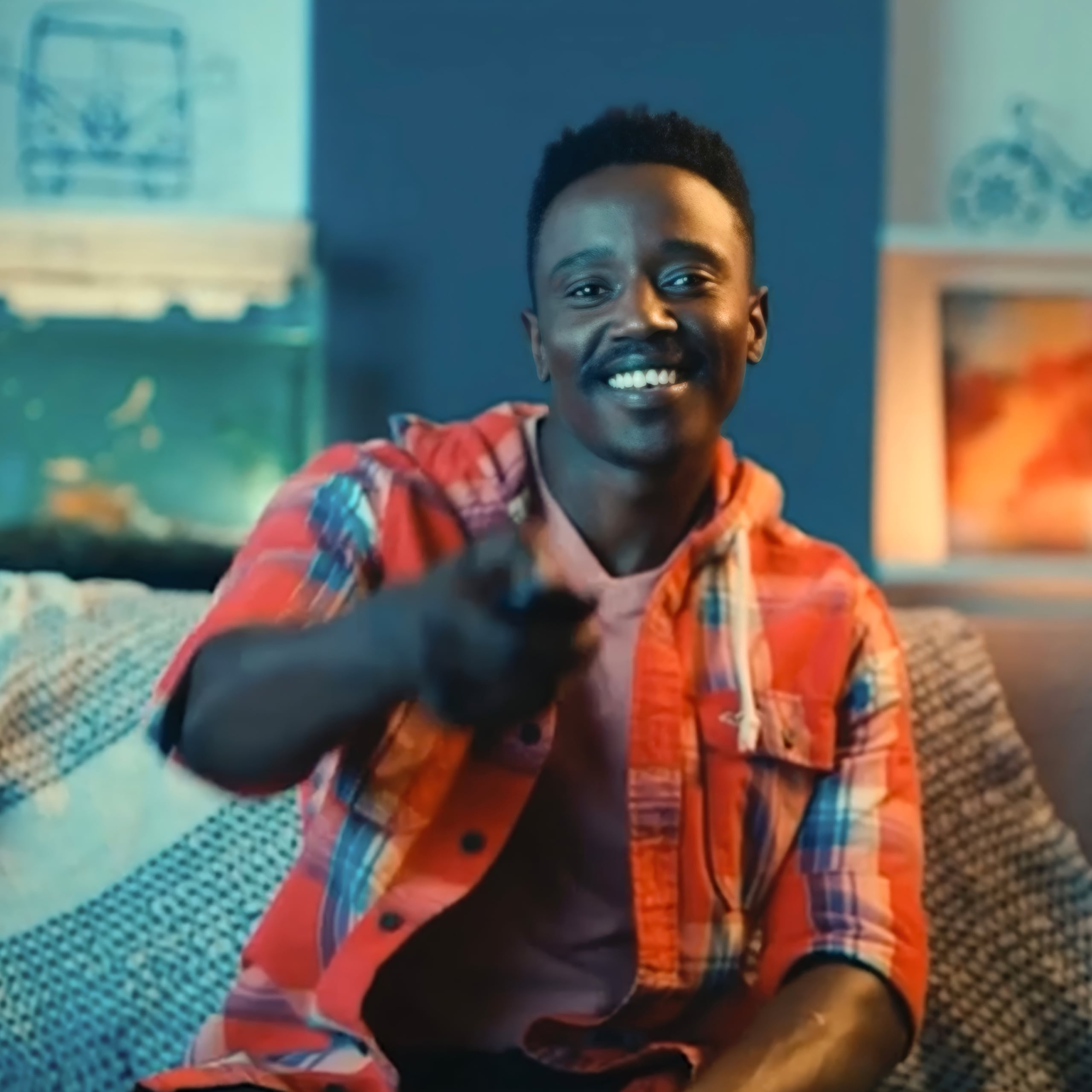 Man sitting on a sofa and smiling while he points a remote control towards the reader