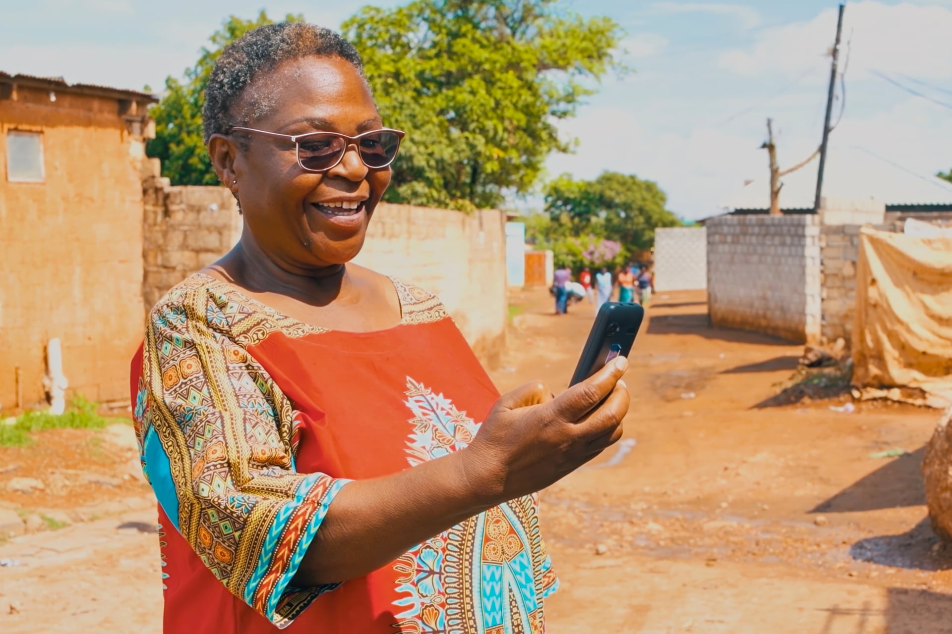 Older lady in sunglasses smiling while looking at her phone