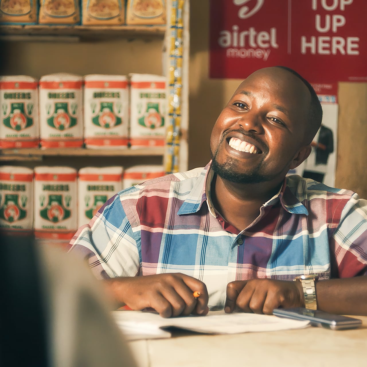 A man in a shop featuring an airtel money sign in the background is smiling at the person opposite him
