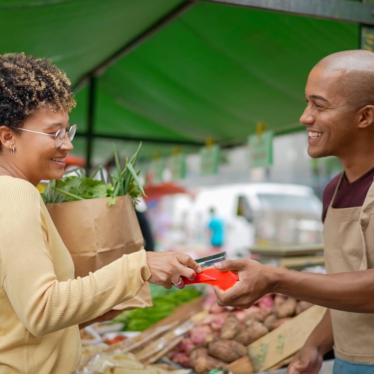 Woman buying groceries from a stall holder, using a card reader