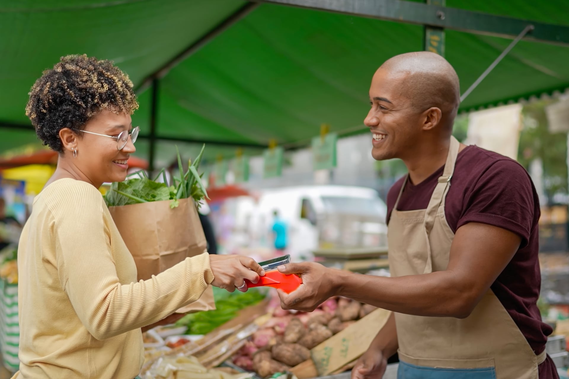 Woman tapping her phone to pay a salesman at a market stall
