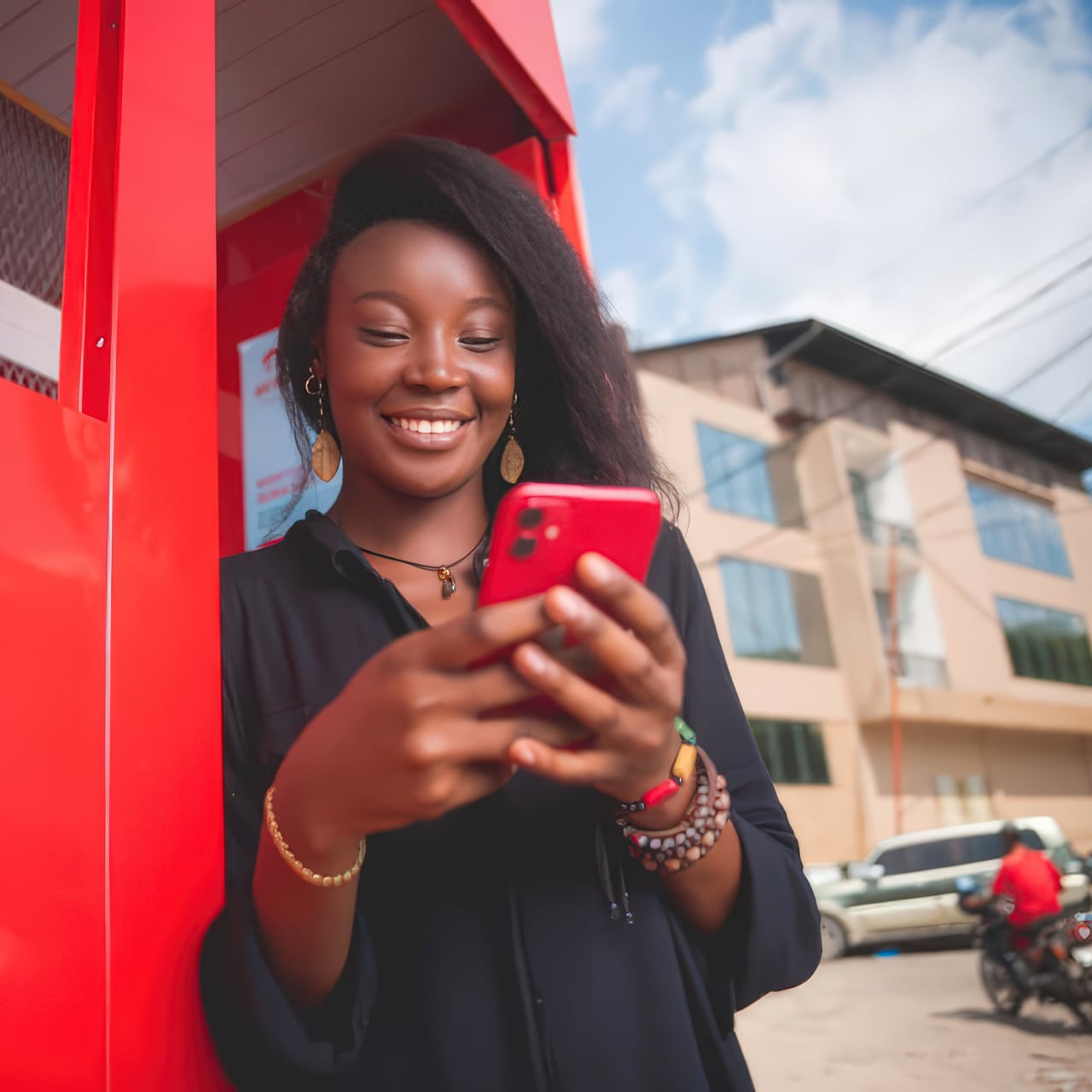 Young woman leaning in a red doorway, looking down at the phone in her hands