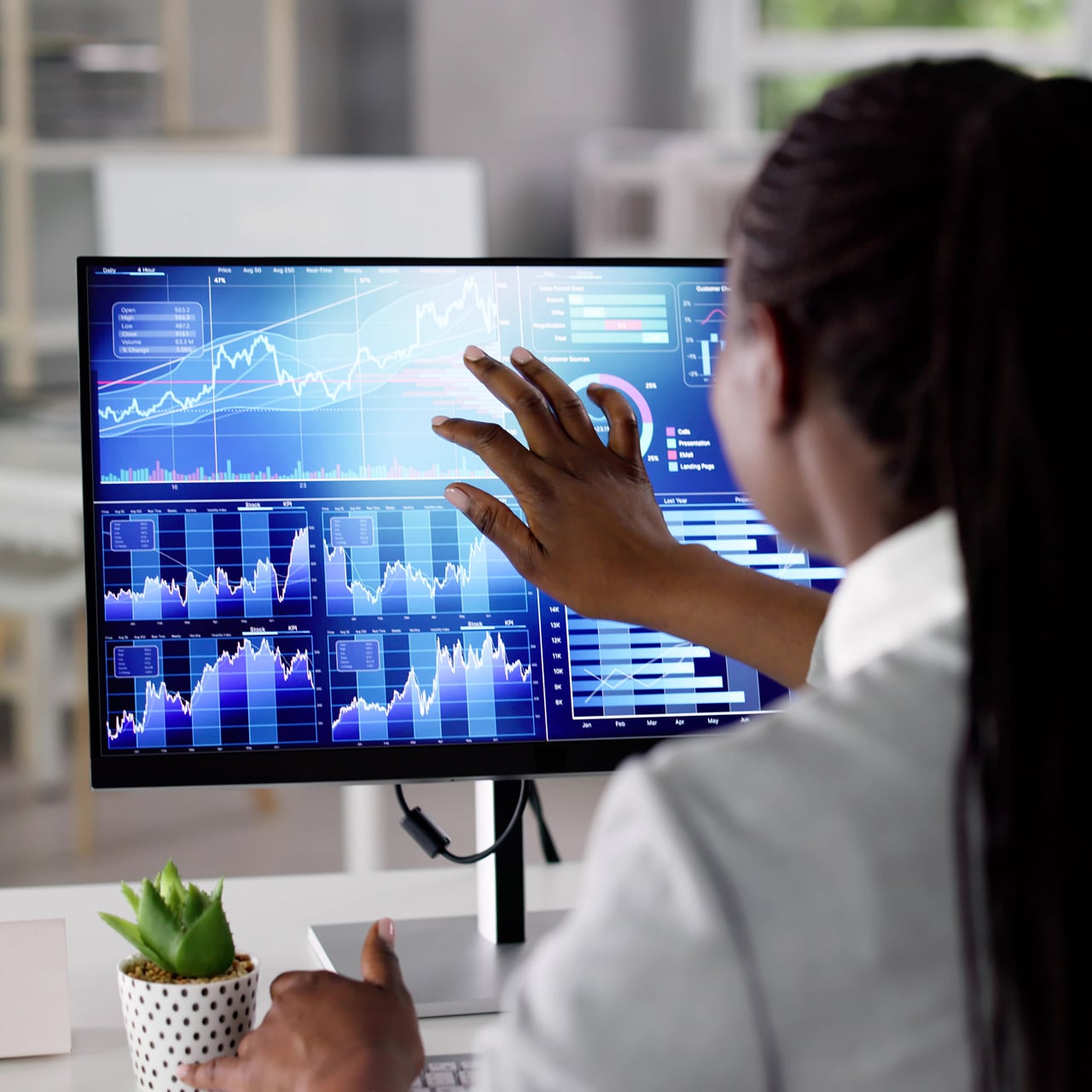 A woman tapping the screen of a computer displaying charts