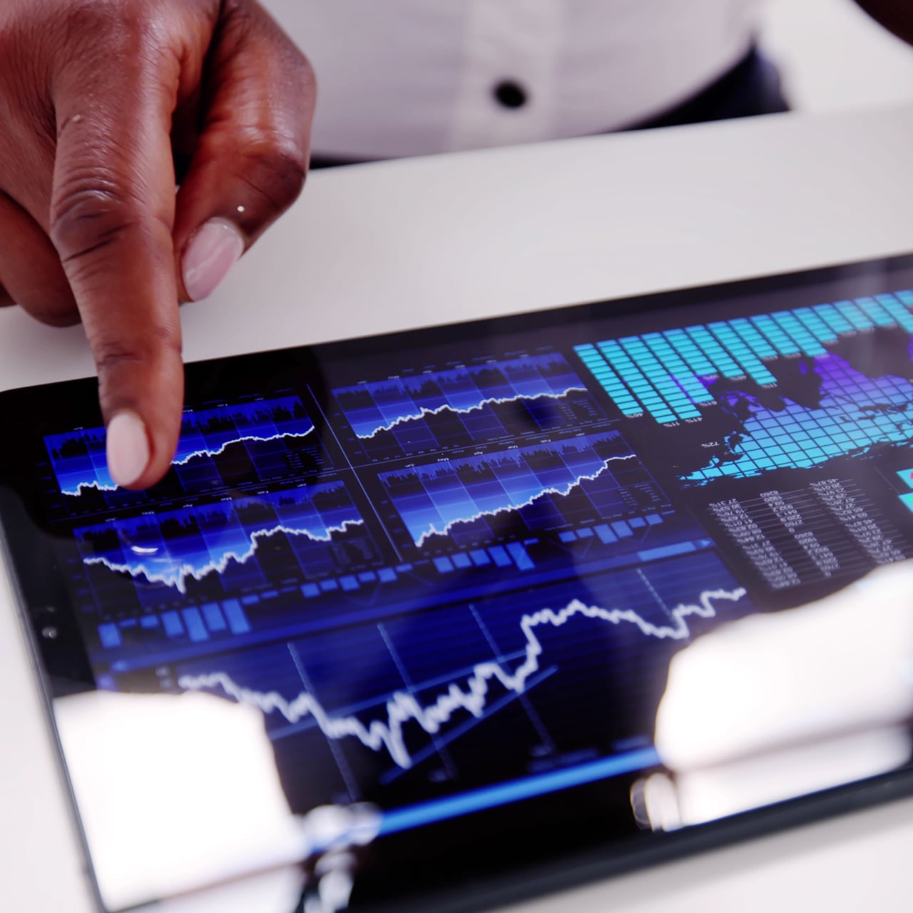 A hand pointing at the screen of a tablet displaying charts