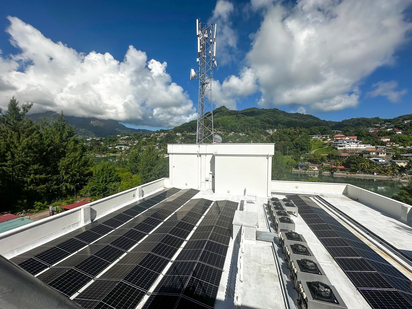 Solar panels placed across a flat roof with a view of green hills and other houses in the background