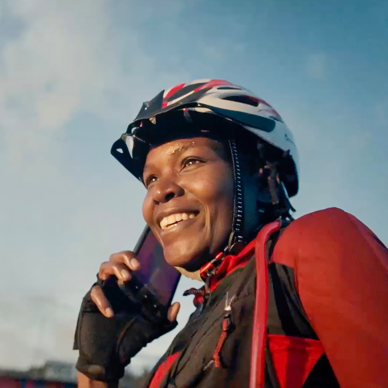 Woman in cycling attire and a helmet holding her phone to her ear while smiling