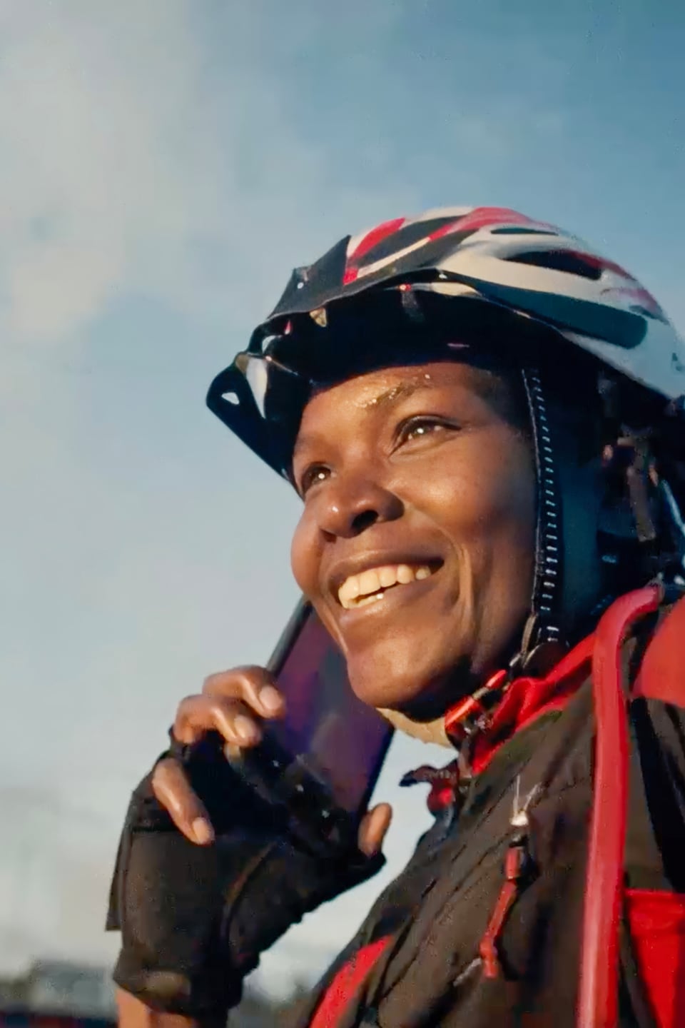Woman in cycling attire and a helmet holding her phone to her ear while smiling
