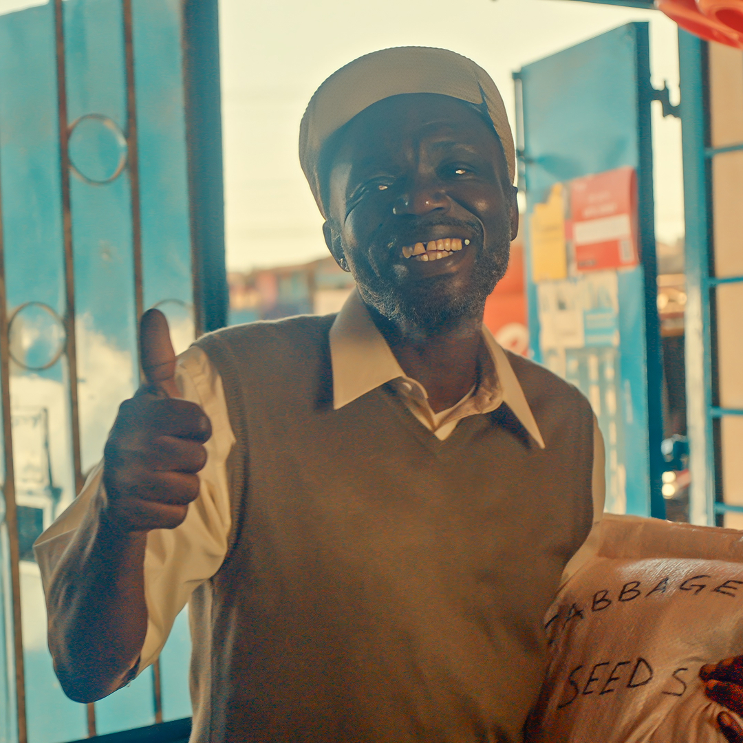 A man smiling while holding a bag of seeds and giving a thumbs up to somebody out of frame