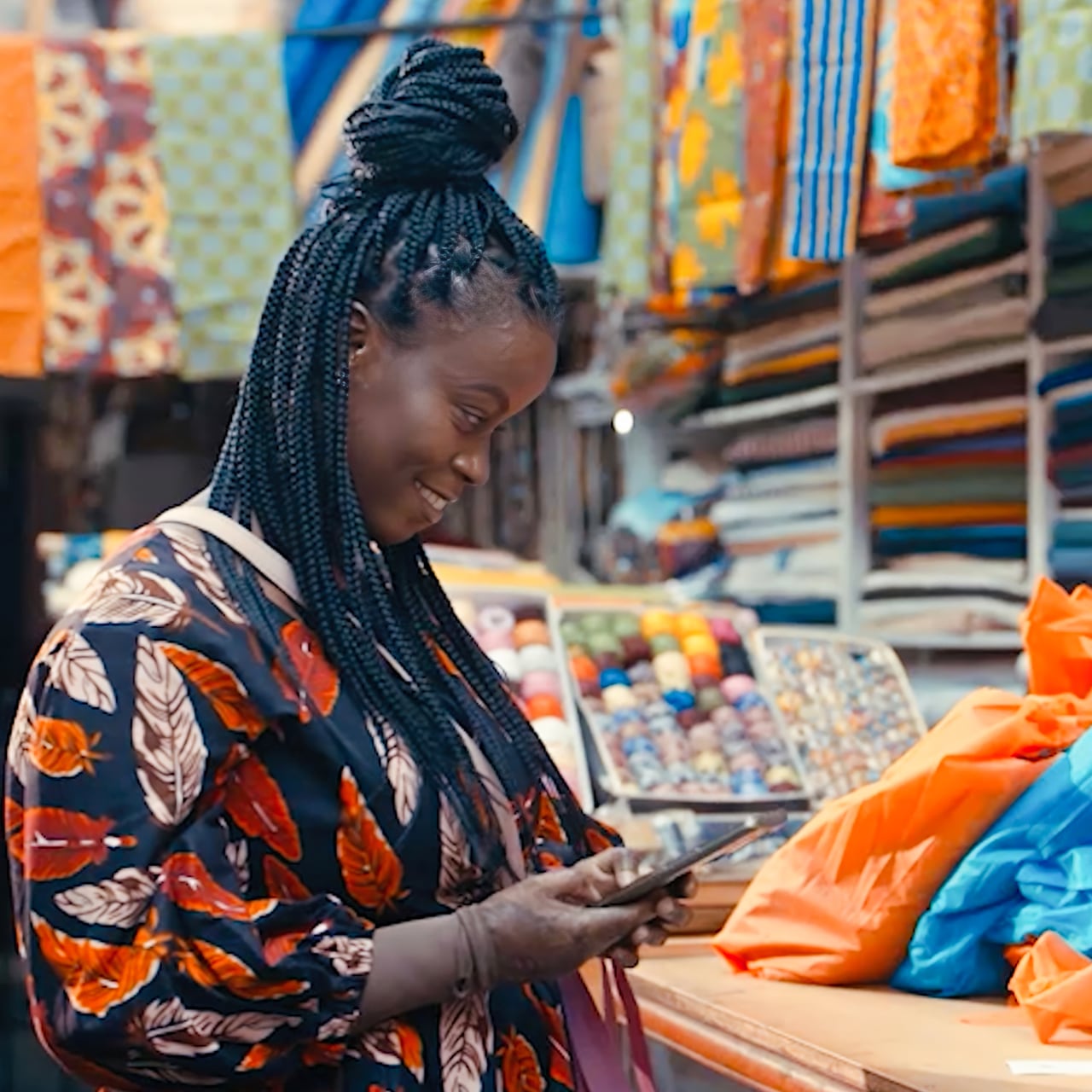 Woman in a fabric shop smiling while looking down at her phone