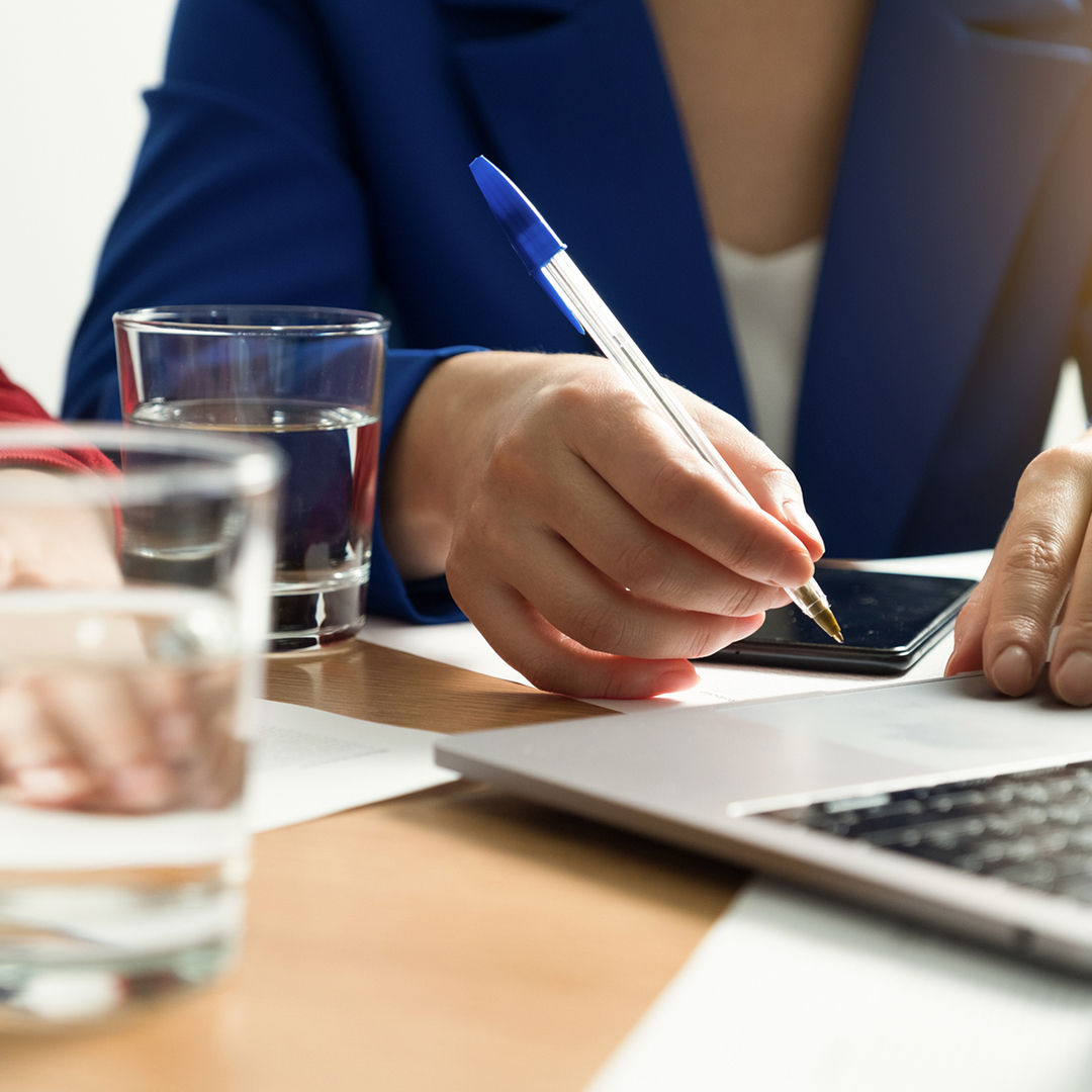A close up of a woman in business attire taking notes on a meeting room table