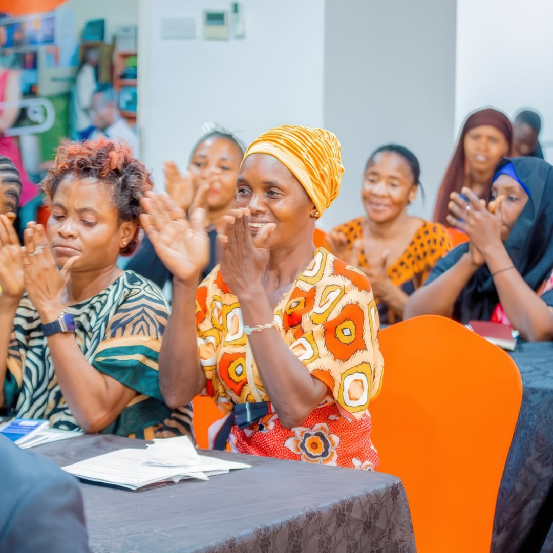 A room of women clapping while they sit at rows of tables at an event