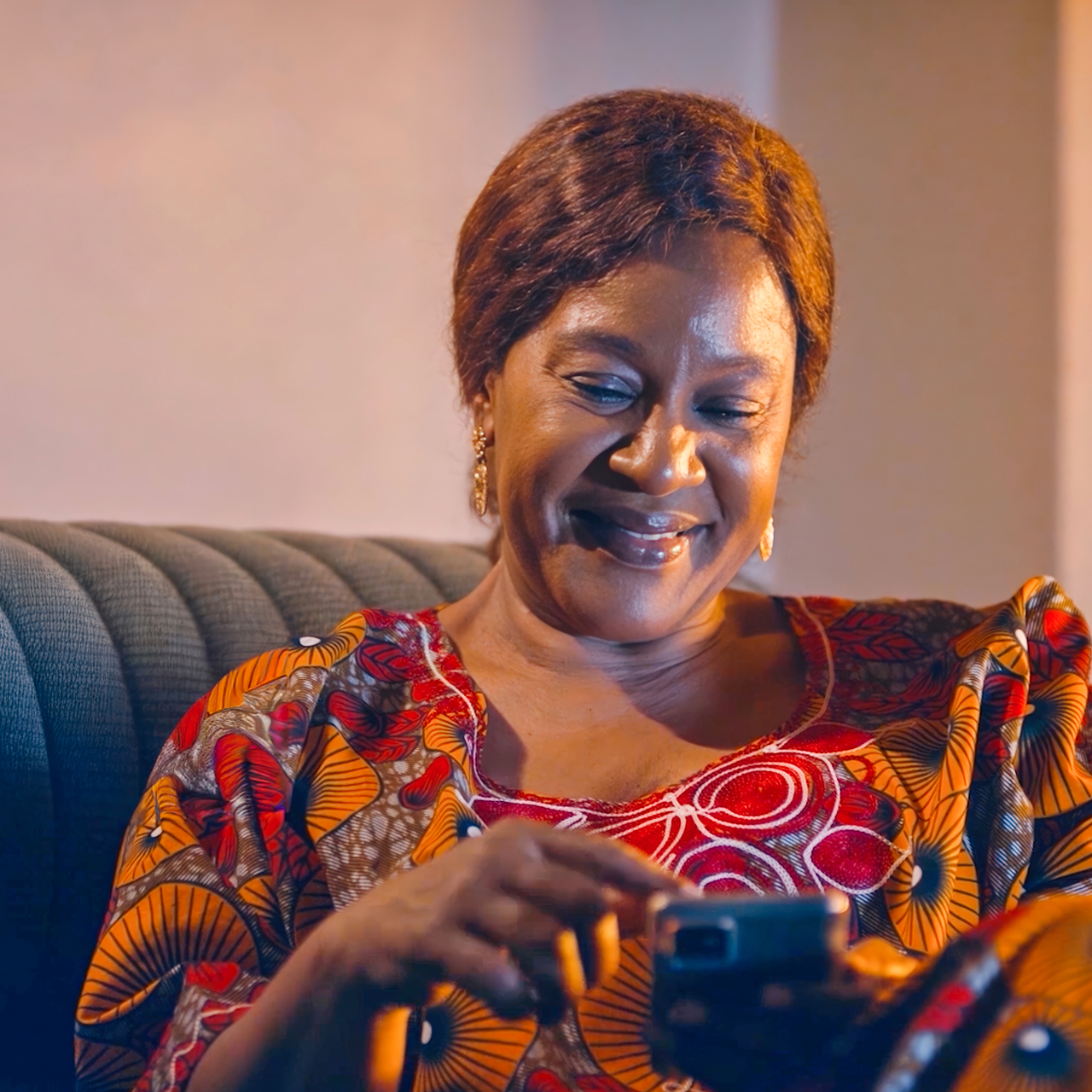 Woman sitting on a sofa looking down at her phone with a relaxed smile