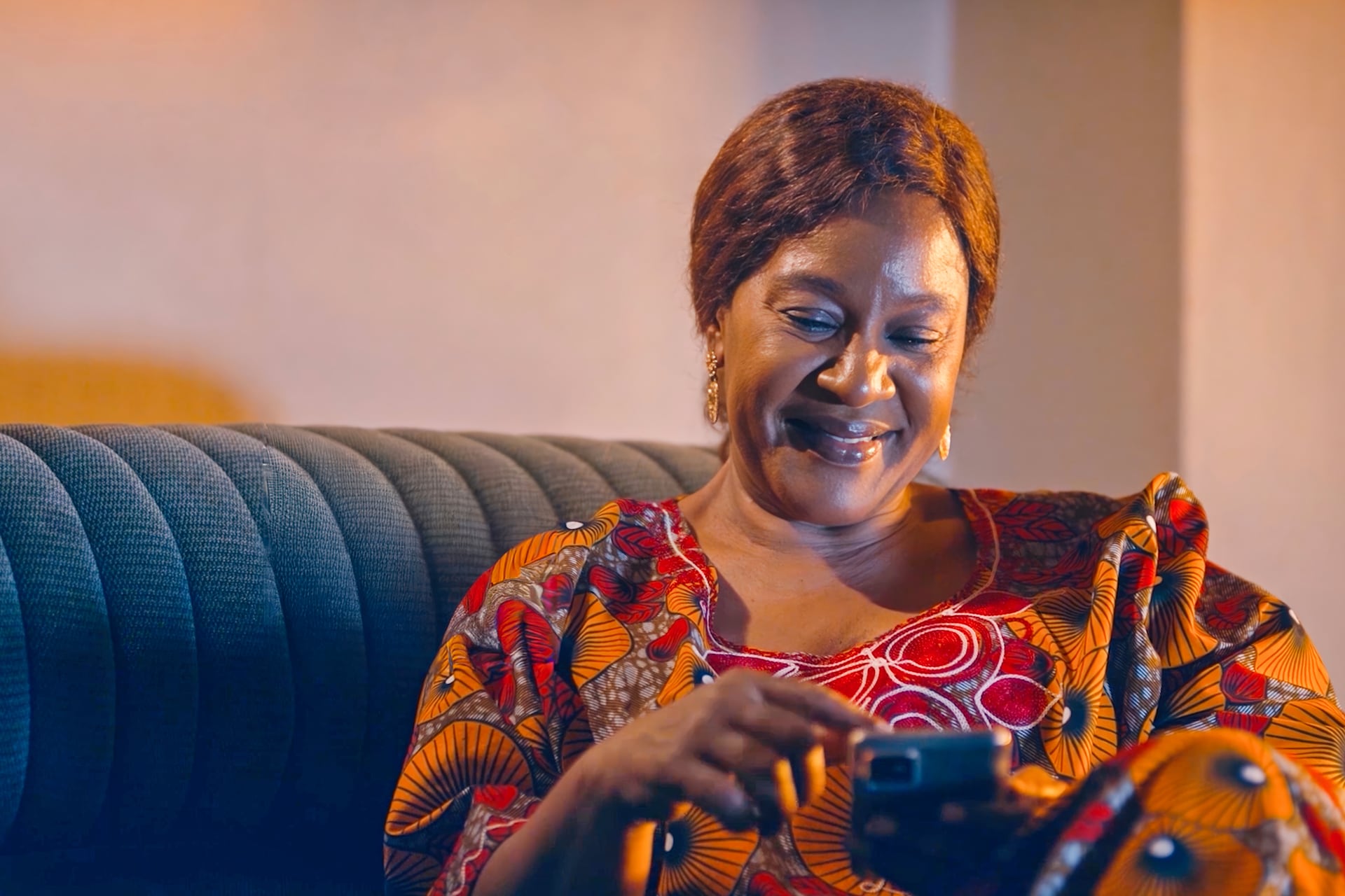 Woman sitting on a sofa looking down at her phone with a relaxed smile