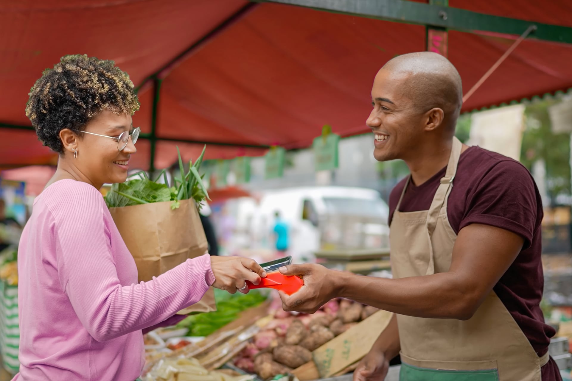 Woman tapping her phone to pay a salesman at a market stall