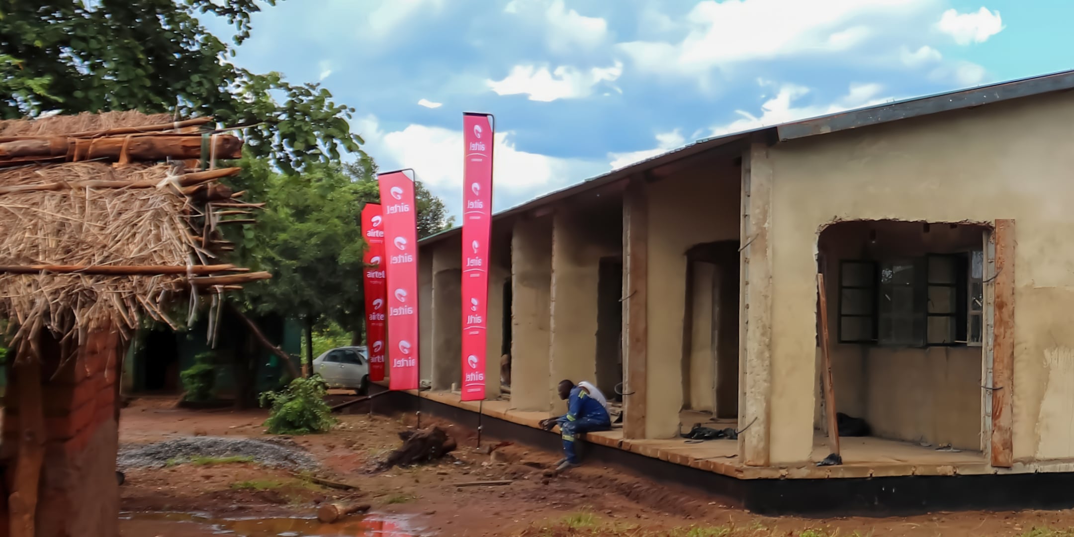 A school building with two men sitting on its porch and Airtel banners set up in front of it