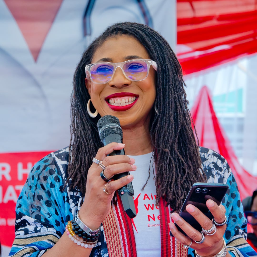 A woman mid-speech, holding a microphone in one hand and a phone in the other